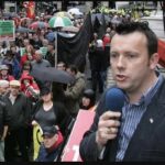 Brendan Ogle speaking into a microphone protesting outside the Dáil in Dublin with a crowd in front
