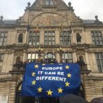 Brendan in Brussels with a banner hanging from a historic building saying Europe it can be Different