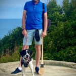 Brendan Ogle, hstanding on a concrete circle with the ocean behind him, with his dog Frida and a hurl
