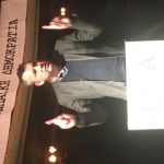 brendan Ogle with fingers in the air addressing a crowd from a podium in front of a sign