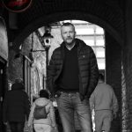 Brendan Ogle looking happy under merchants arch in Dublin, hands in pockets - Black and White photo taken by Martin Blake