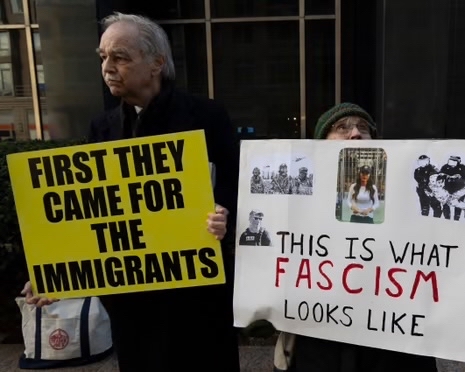 Photo with two protesters holding signs 'First they camme for the immigrants'. and Facism
